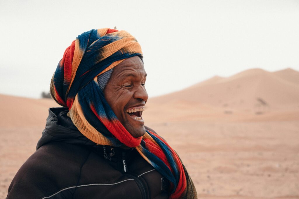 Joyful Bedouin man laughing in the desert, wearing a vibrant headscarf.